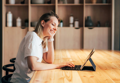 Young woman using phone while sitting on table at home