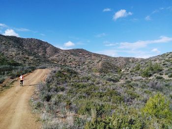 Man walking on road by mountain against sky