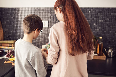 Rear view of brother and sister working at kitchen counter