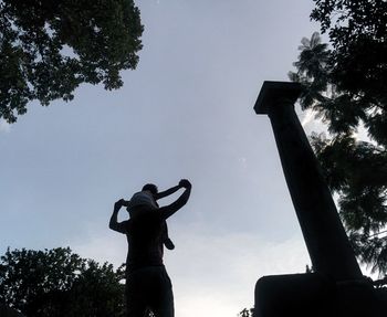 Low angle view of man standing by tree against sky