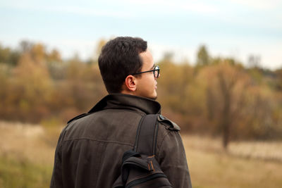 Back view tourist adventurous man with backpack stands on fall nature background. man enjoys 