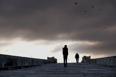 Silhouette people walking against cloudy sky