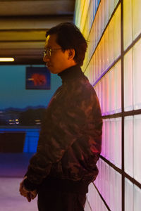 Young man standing against illuminated wall