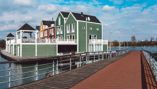 View of pier over river by buildings against sky