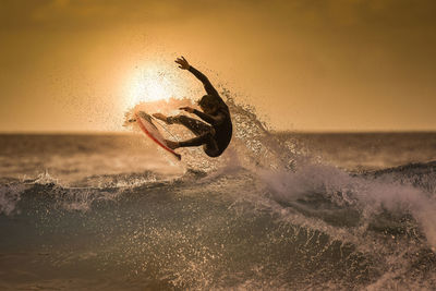 Teenage boy surfing in sea against sky during sunset