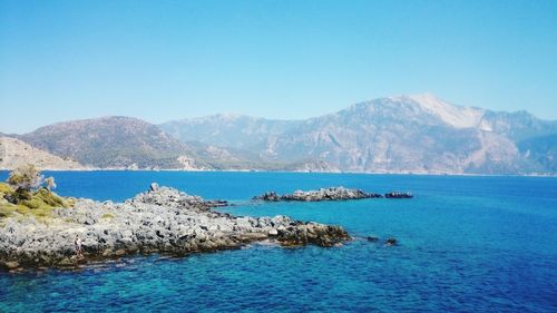 Scenic view of sea by mountains against clear sky