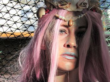 Close-up portrait of woman with dyed long pink hair against net