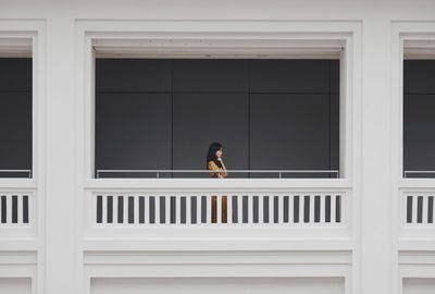 Young woman standing by railing against wall