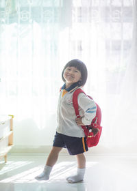 Full length of smiling girl standing against window