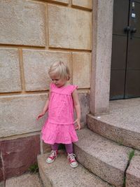 Blond girl standing on steps against wall