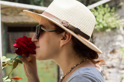 Close-up portrait of young woman wearing sunglasses and smelling rose. 