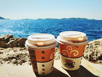 Close-up of disposable cups by sea against sky