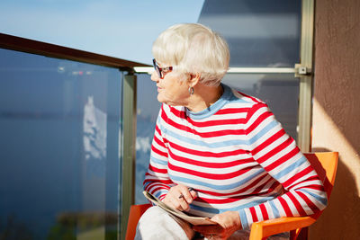 Senior woman in glasses sitting on balcony near the sea