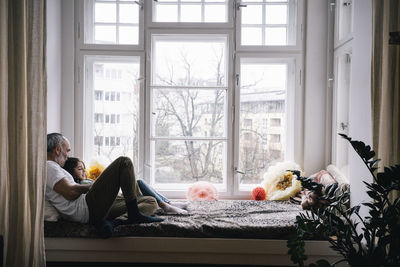 Father and daughter sitting together on alcove window seat at home