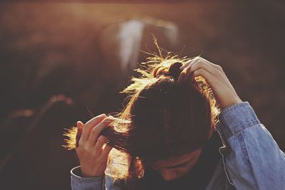 Close-up of young woman tying hair while standing outdoors during sunset