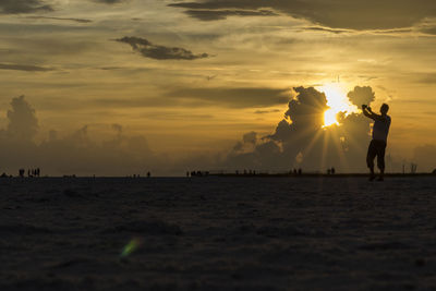 Silhouette people standing on beach against sky during sunset