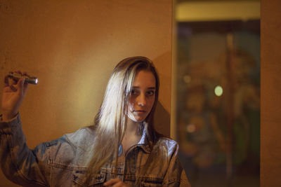 Portrait of beautiful young woman holding flashlight against wall at night