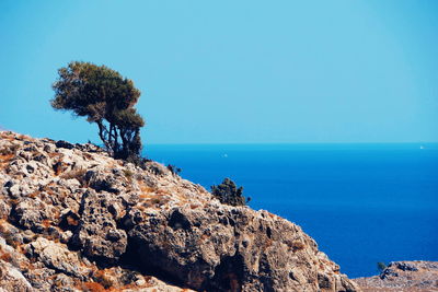 Rocks by sea against clear blue sky