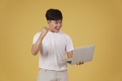 Young man using mobile phone against yellow background