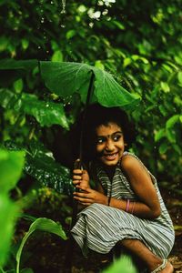 Smiling cute girl crouching amidst plants in rain