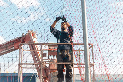 Man photographing through fence against sky