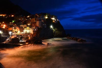 Illuminated buildings by sea against sky at night