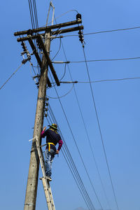 Low angle view of electrician repairing power lines against clear sky