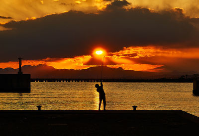 Silhouette people standing on beach against sky during sunset