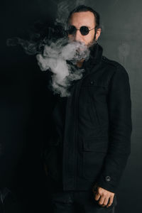 Portrait of man smoking cigarette while standing against wall