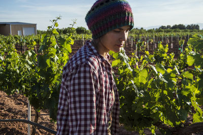 Woman wearing knit hat looking down while standing by agriculture field