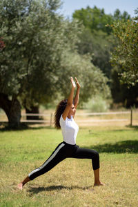 Woman stretching body on field against trees