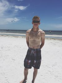 Portrait of smiling young man in sunglasses standing at beach during sunny day