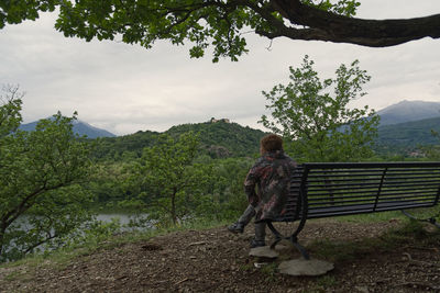 A caucasian girl sitting on a bench by the lake looks at the mountains in a cloudy day person