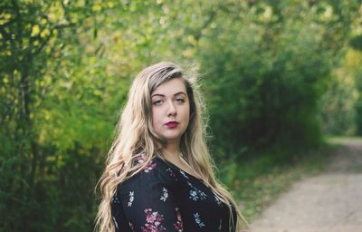 Portrait of beautiful young woman standing against trees