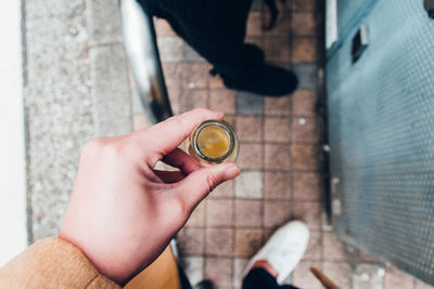 Low section of man holding bottle while standing on footpath