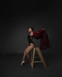 Side view of young woman sitting against black background