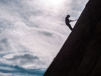 Low angle view of silhouette man climbing on mountain against sky