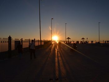 People walking in city against clear sky during sunset