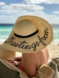 Close-up of woman with text on hat relaxing at beach against sky