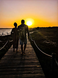 Rear view of silhouette men standing on railing against sky during sunset