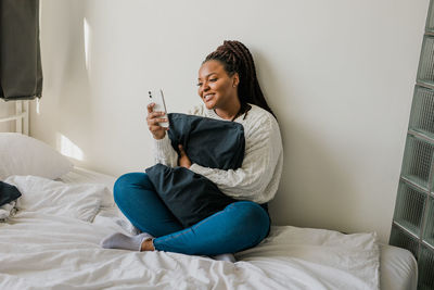 Young woman using mobile phone while lying on bed at home