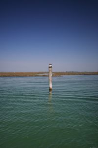 Lighthouse by sea against clear blue sky