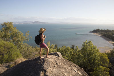 Woman standing on rock by sea against sky