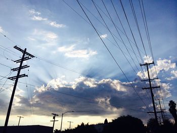 Low angle view of electricity pylon against cloudy sky