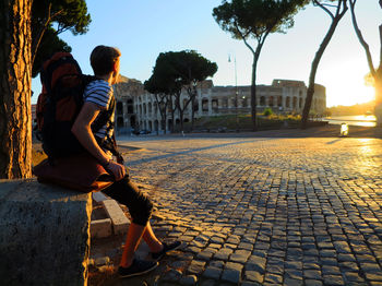 Man sitting on street against sky in city