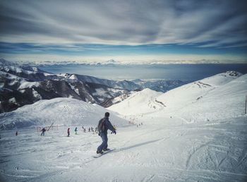 Snowboarder skiing on snowcapped mountain against sky