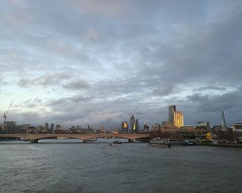 View of buildings by river against cloudy sky