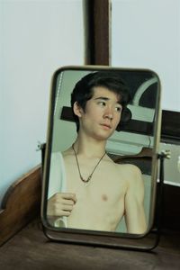 Shirtless teenage boy reflecting on mirror