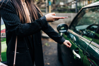 Unrecognizable long-haired woman opening a car with mobile phone
