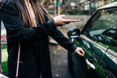 Unrecognizable long-haired woman opening a car with mobile phone